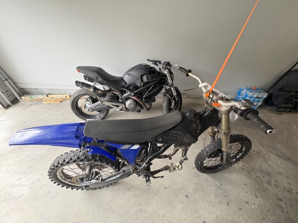 The crashed Ducati Monster 696 and the YZ450F chassis side by side in the garage