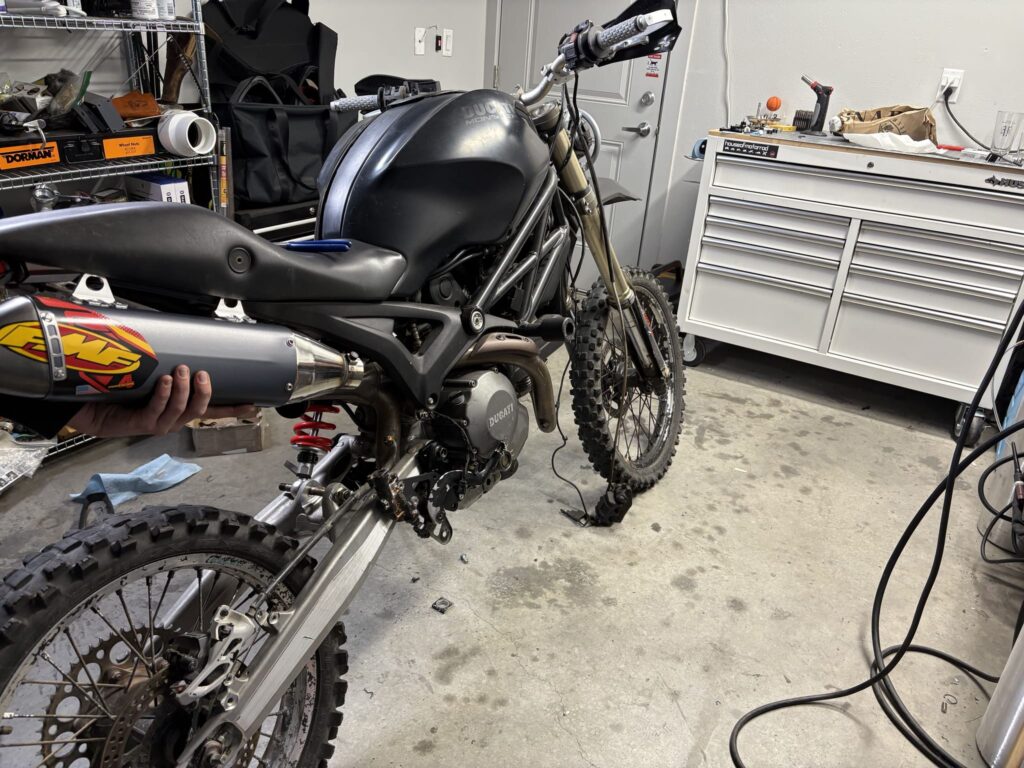 Holding an FMF muffler up to the left side of the bike